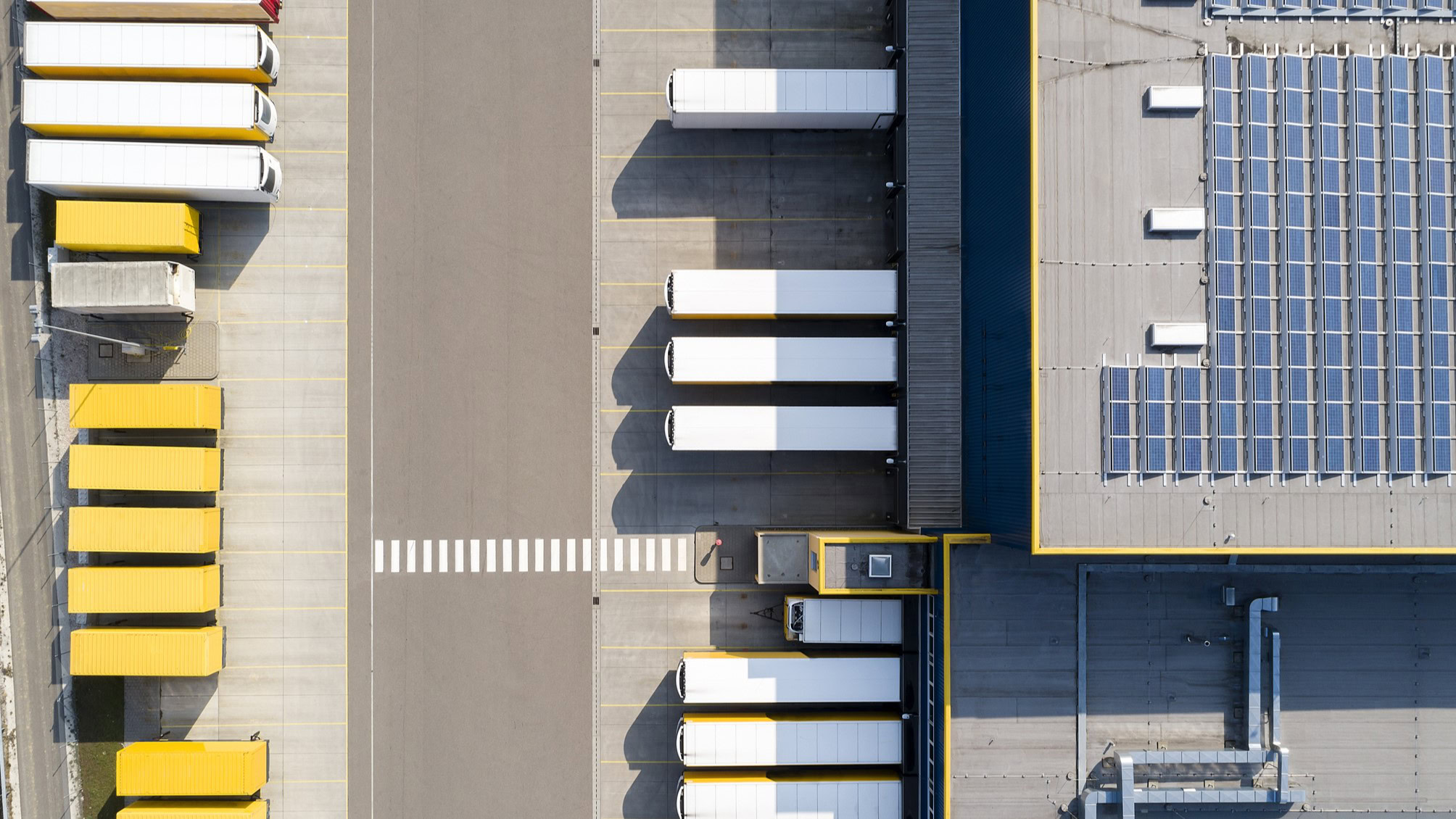 Aerial view of a distribution center with parked trucks in yellow and white, aligned neatly beside the loading docks.