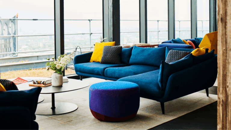 Modern living room with a blue sectional sofa, colorful pillows, coffee table, and city view through large windows.