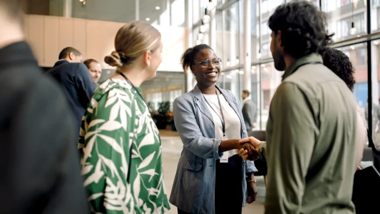People networking and shaking hands in a modern, glass-walled conference setting.