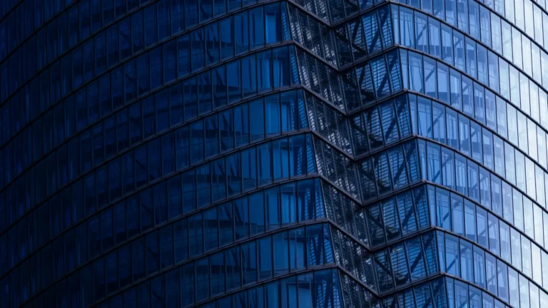 Close-up view of a modern glass skyscraper façade with repeating blue-tinted windows and diagonal architectural lines creating a geometric pattern.