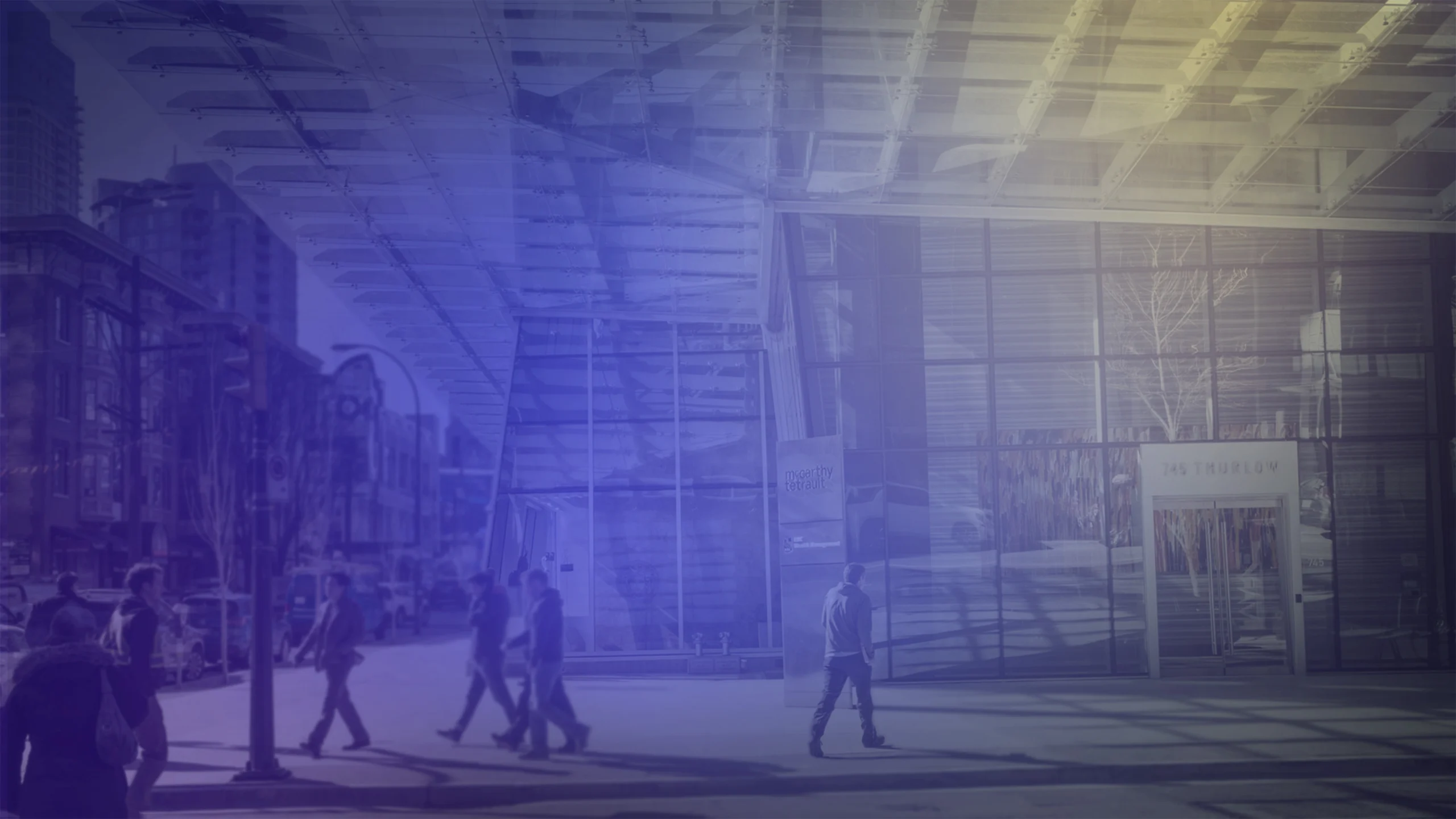 Modern glass office building entrance on a city street, with pedestrians crossing and walking along the sidewalk; the scene is overlaid with a blue gradient.