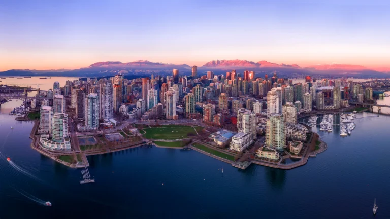 Vue aérienne du centre-ville de Vancouver au coucher du soleil, avec les montagnes en arrière-plan et le front de mer au premier plan.