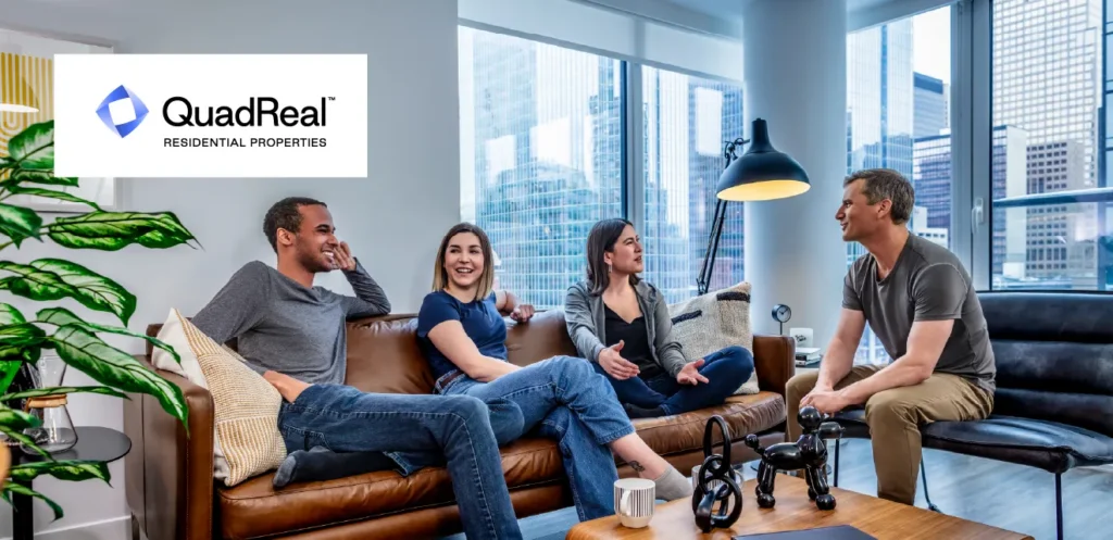 Four residents sitting and talking in a bright apartment lounge with floor-to-ceiling windows overlooking a city skyline, with the QuadReal Residential Properties logo displayed in the upper left corner.