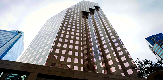 Low-angle view of a tall, modern office tower with a grid of reflective windows, rising against a pale sky.