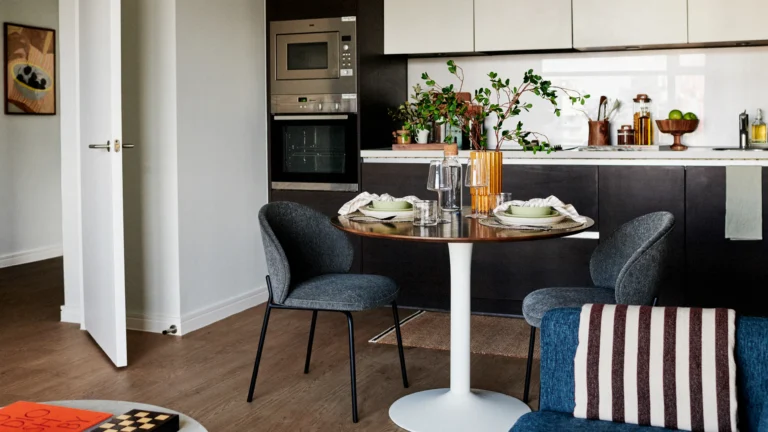 Modern kitchen and dining nook with a round table set for two and contemporary cabinetry.