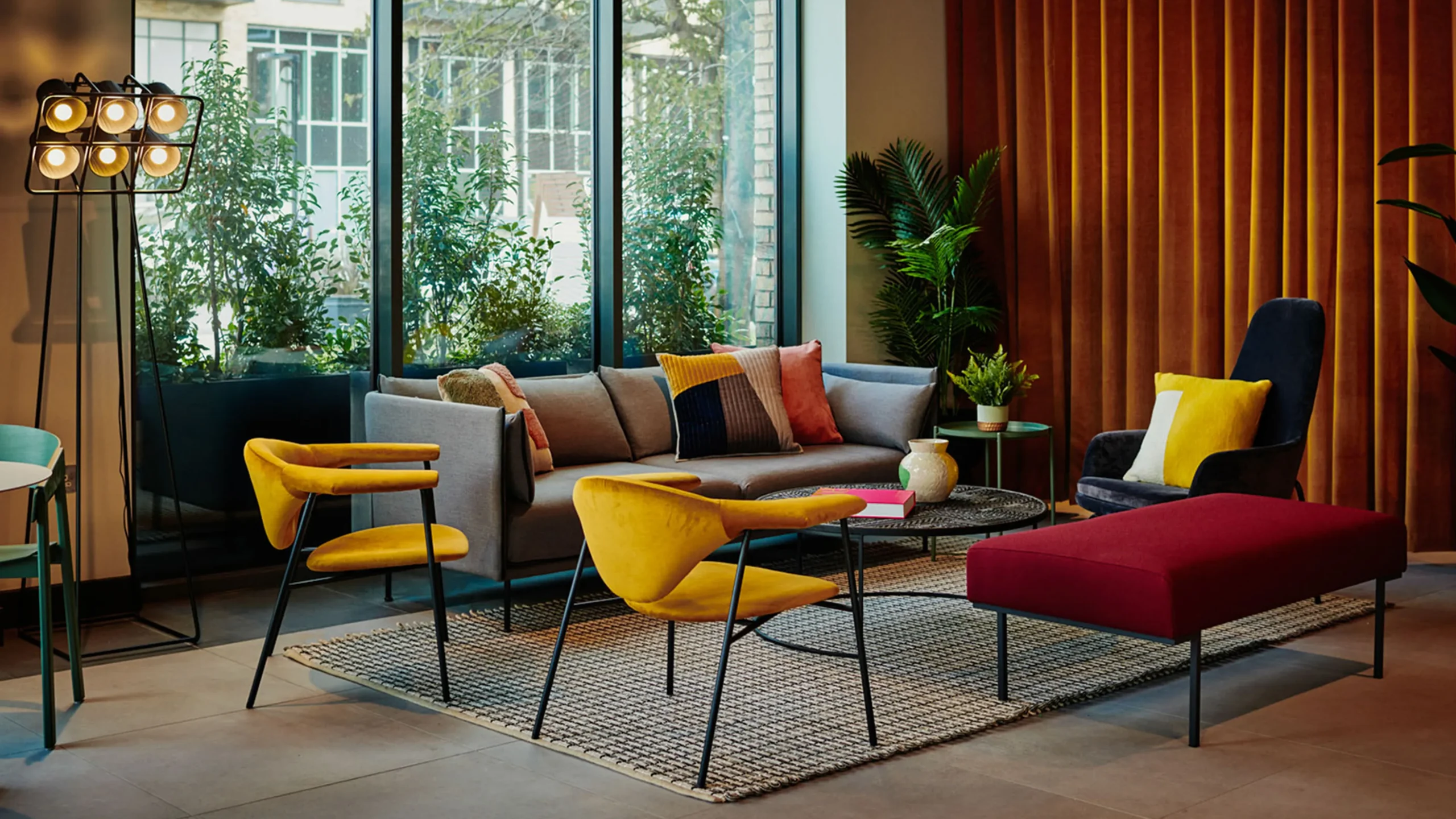 Modern resident lounge with floor-to-ceiling windows, a grey sofa, colourful accent chairs and soft seating areas, creating a bright and welcoming communal space