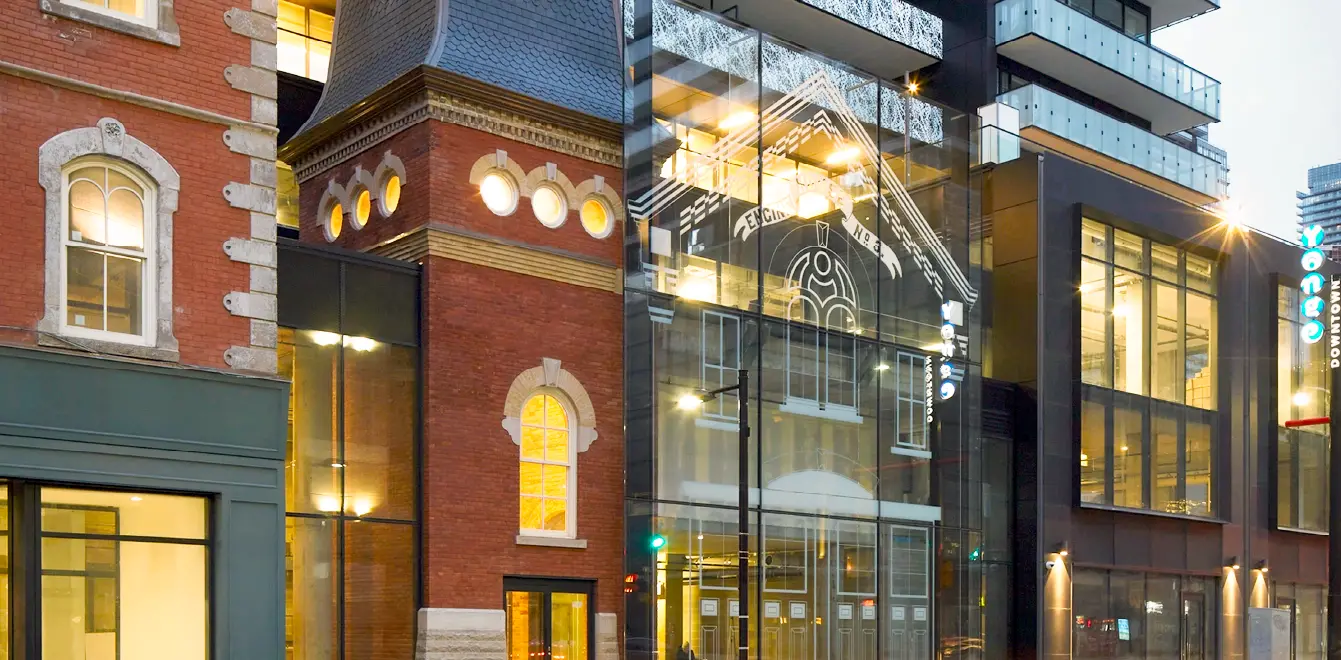 Heritage brick building and modern glass office tower illuminated at dusk.
