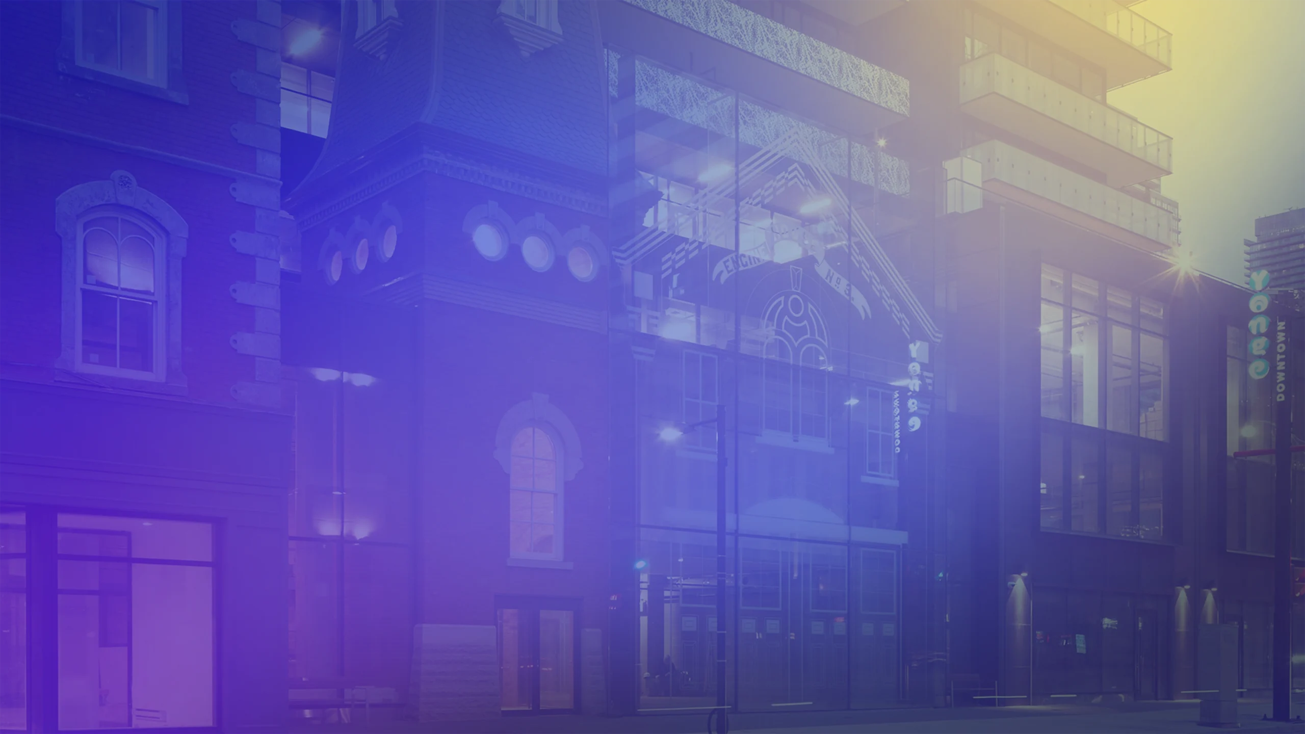Modern mixed-use building with a glass façade integrated into a historic brick structure at street level, illuminated at dusk. A blue and purple gradient overlay softens the image, with balconies visible on the upper floors and storefront windows along the sidewalk.