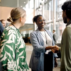 Personnes réseautant et se serrant la main dans un cadre de conférence moderne avec des murs en verre.