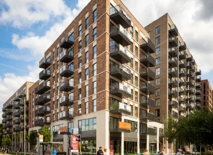 Exterior view of a modern brick apartment building with private balconies, ground-floor retail space and landscaped streetscape in an urban neighbourhood.