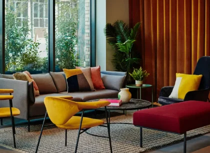 Modern resident lounge with floor-to-ceiling windows, a grey sofa, colourful accent chairs and soft seating areas, creating a bright and welcoming communal space