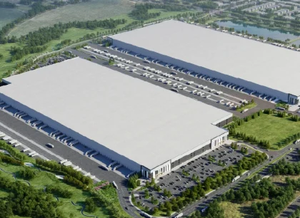 Aerial view of a modern industrial logistics facility featuring two large warehouse buildings, truck loading areas, parking lots, and surrounding green space.