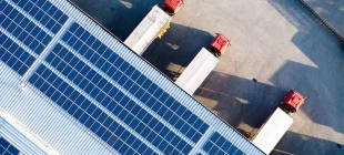 Aerial view of a solar-panel-covered warehouse roof with red trucks at loading docks.