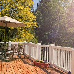 A wooden deck with a patio umbrella and chairs surrounded by trees.